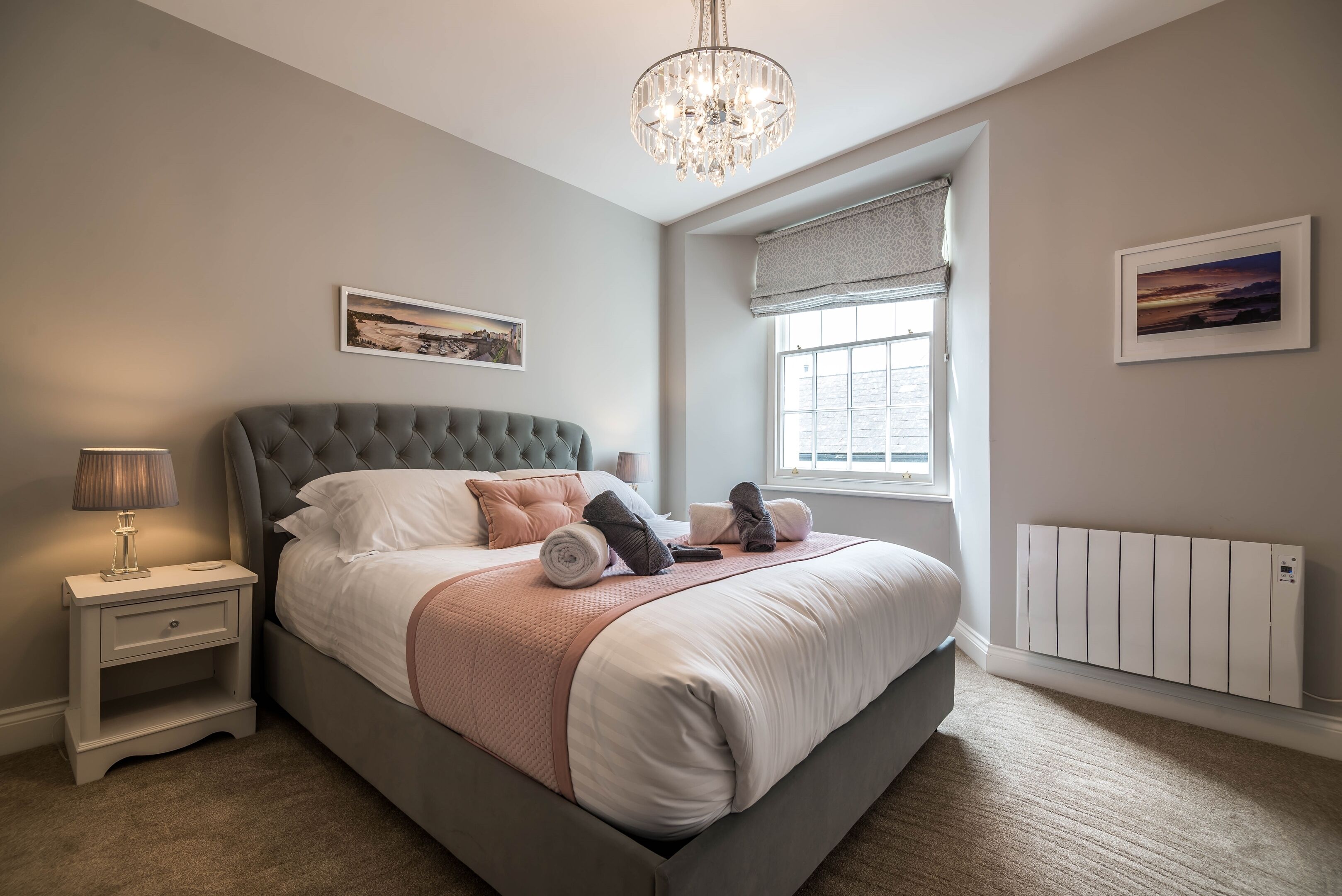 A bedroom with a large bed, a nightstand, a lamp, a radiator, and a window with a view.