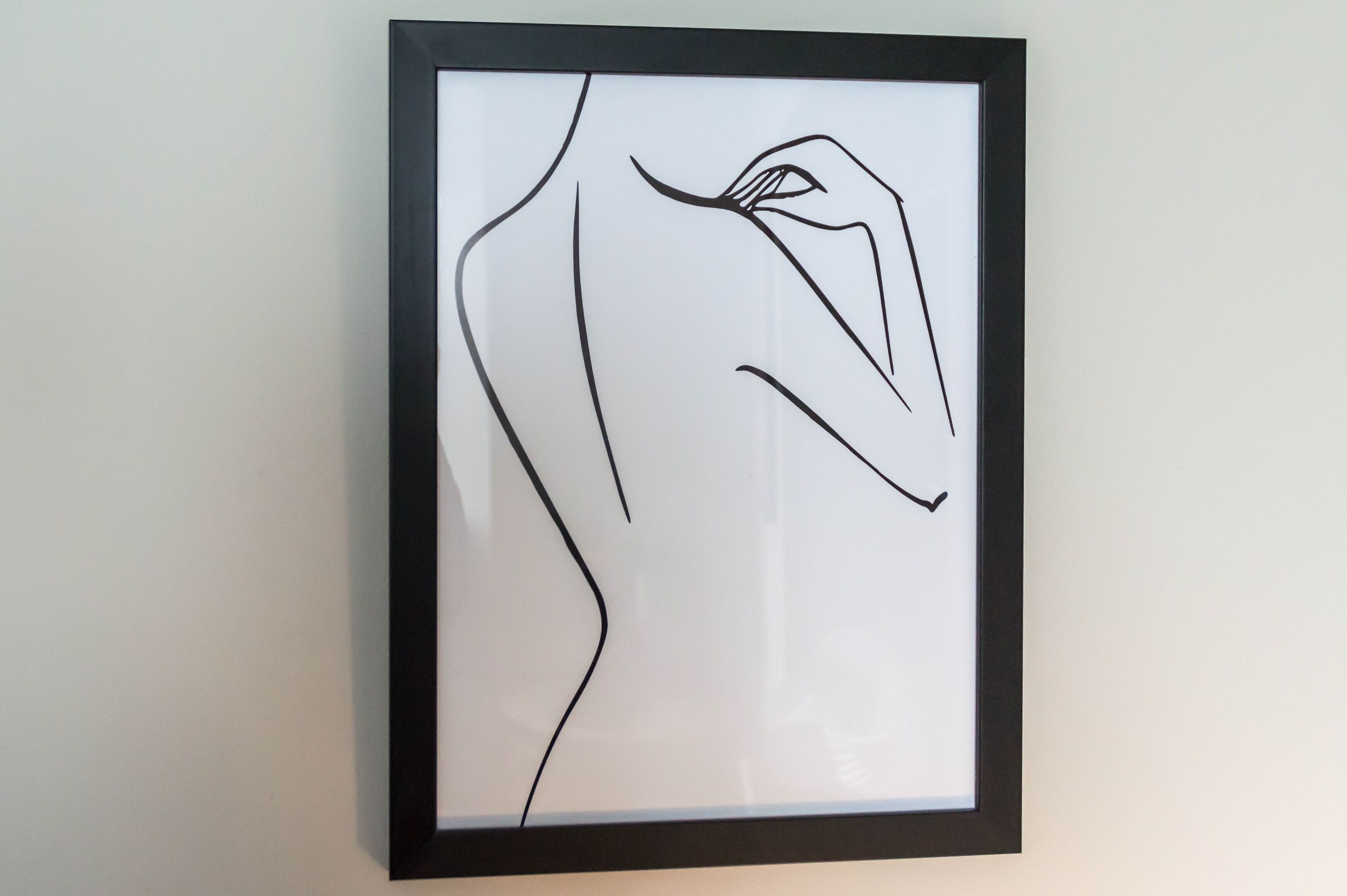 A framed abstract line drawing on a plain wall.