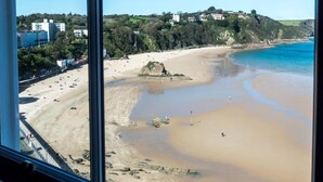 A beach with clear blue water, sandy shore, and a view of buildings in the background. - Lady Tenby - 2 Bedroom Luxury Apartment (Tenby)