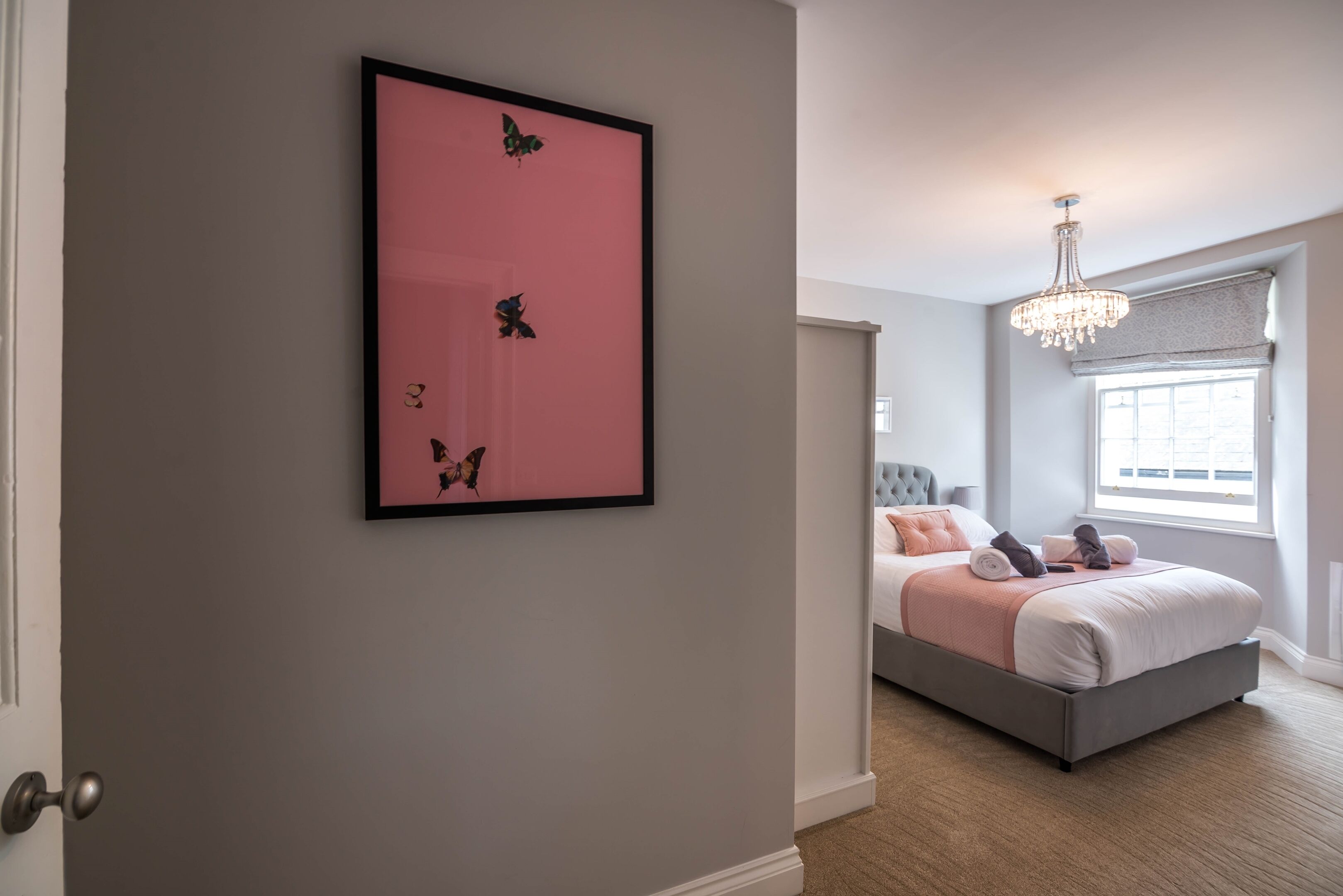Un dormitorio con una cama, una araña de cristal y una obra de arte con mariposas enmarcada en la pared.