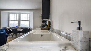 A modern kitchen with a large sink, a dining area with chairs, and a view of the city through large windows. - Lady Tenby - 2 Bedroom Luxury Apartment (Tenby)