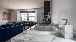 A modern kitchen with a marble countertop, a built-in sink, and a window with a view of the mountains. - Lady Tenby - 2 Bedroom Luxury Apartment (Tenby)