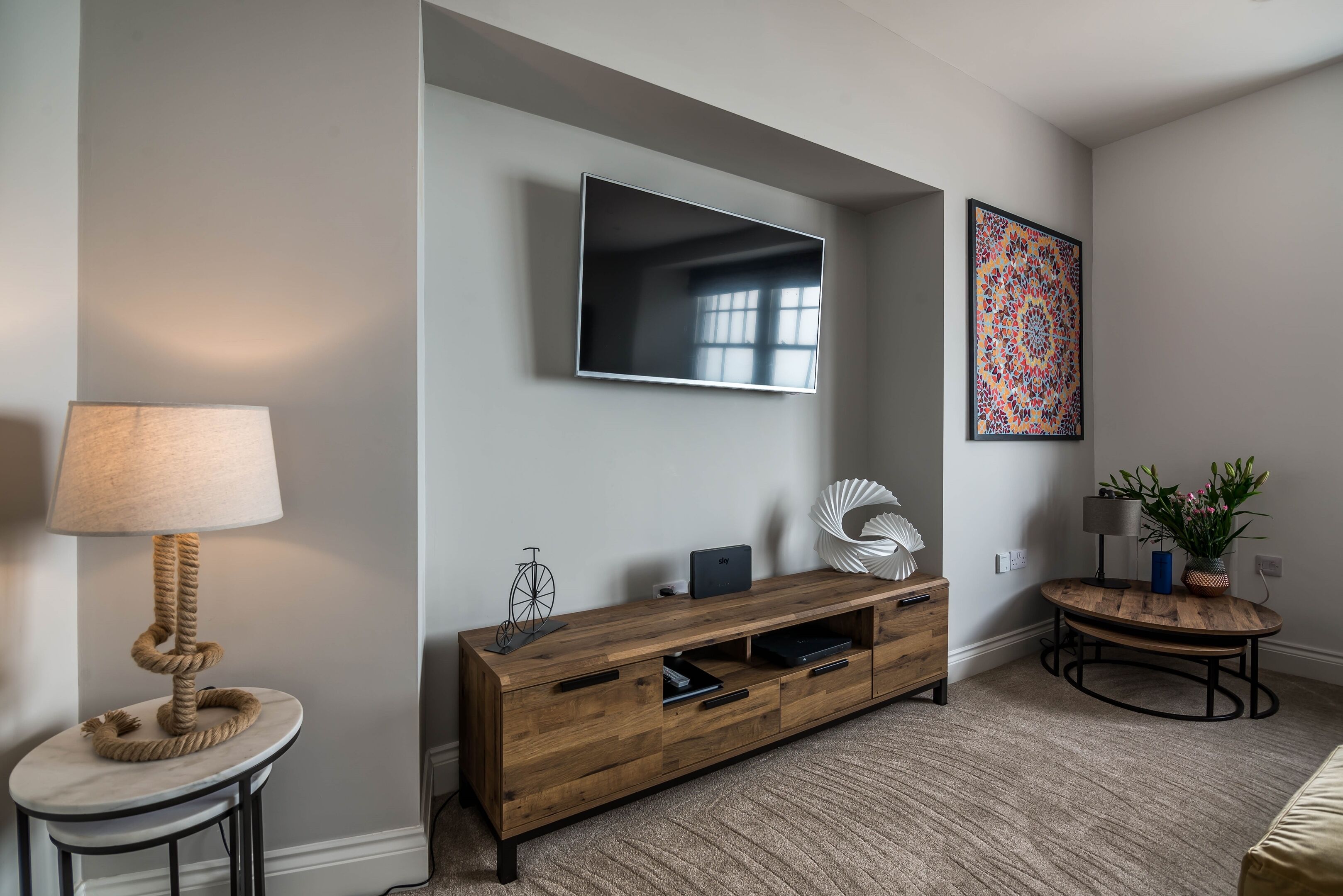 A modern living room with a flat-screen TV, a wooden entertainment unit, a round coffee table, and a potted plant.