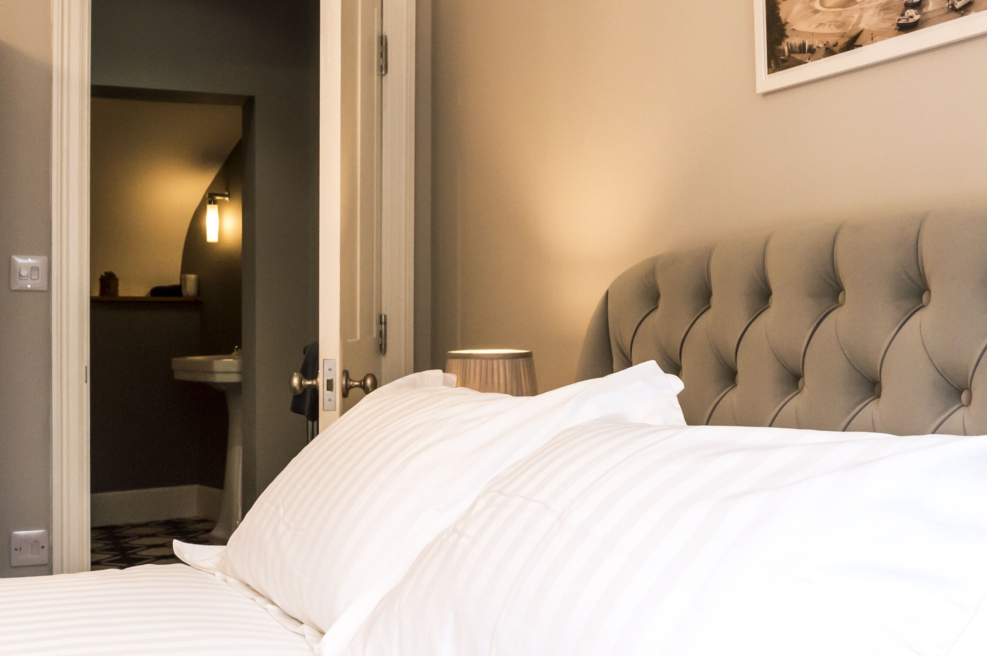 Ein Hotelzimmer mit Bett, einer Nachttischlampe und einem gerahmten Bild an der Wand.