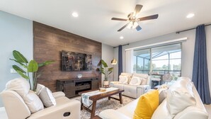 A modern living room with a sofa, coffee table, and a ceiling fan. - Fascinating 5 BR Home Near Disney 8931 (Kissimmee)
