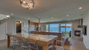 Una cocina moderna con una mesa de comedor y sillas de vidrio, una chimenea y vista al mar.
