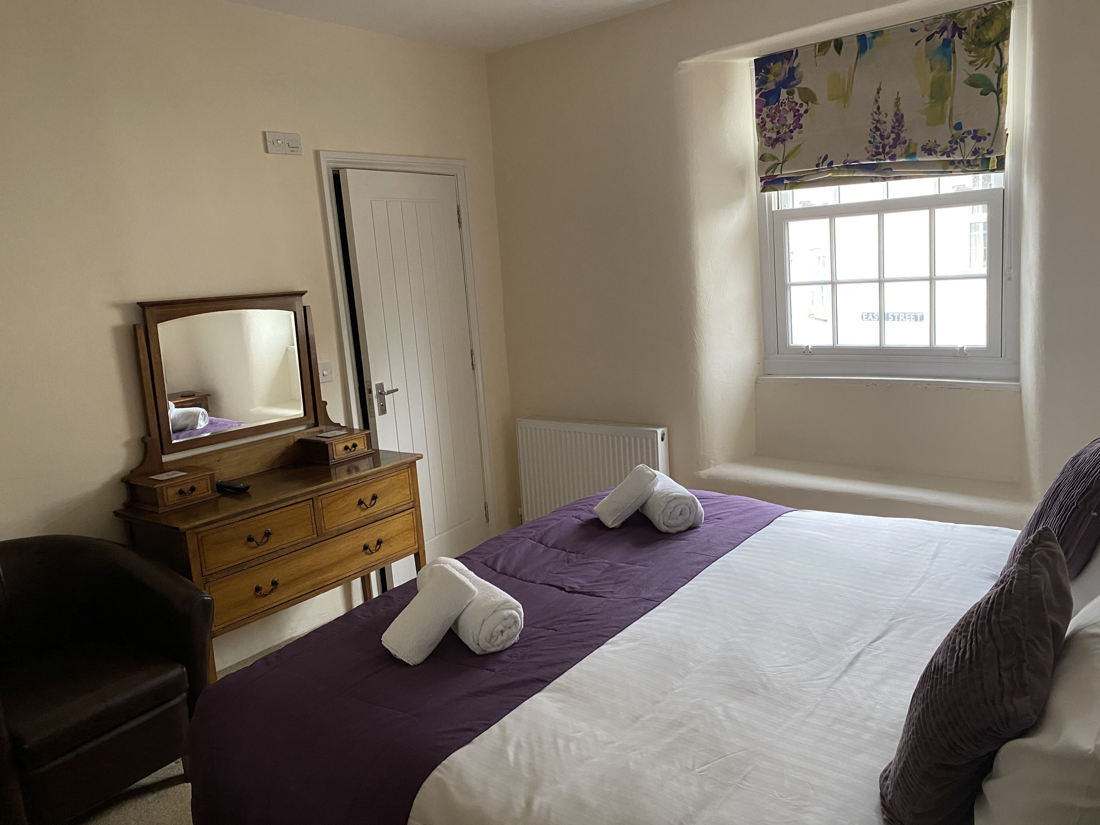 Un dormitorio con cama, cómoda, espejo, ventana y radiador.