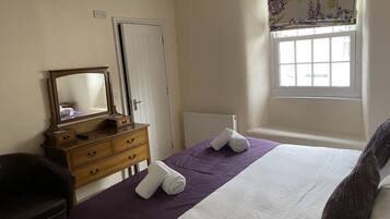 Un dormitorio con cama, cómoda, espejo, ventana y radiador.