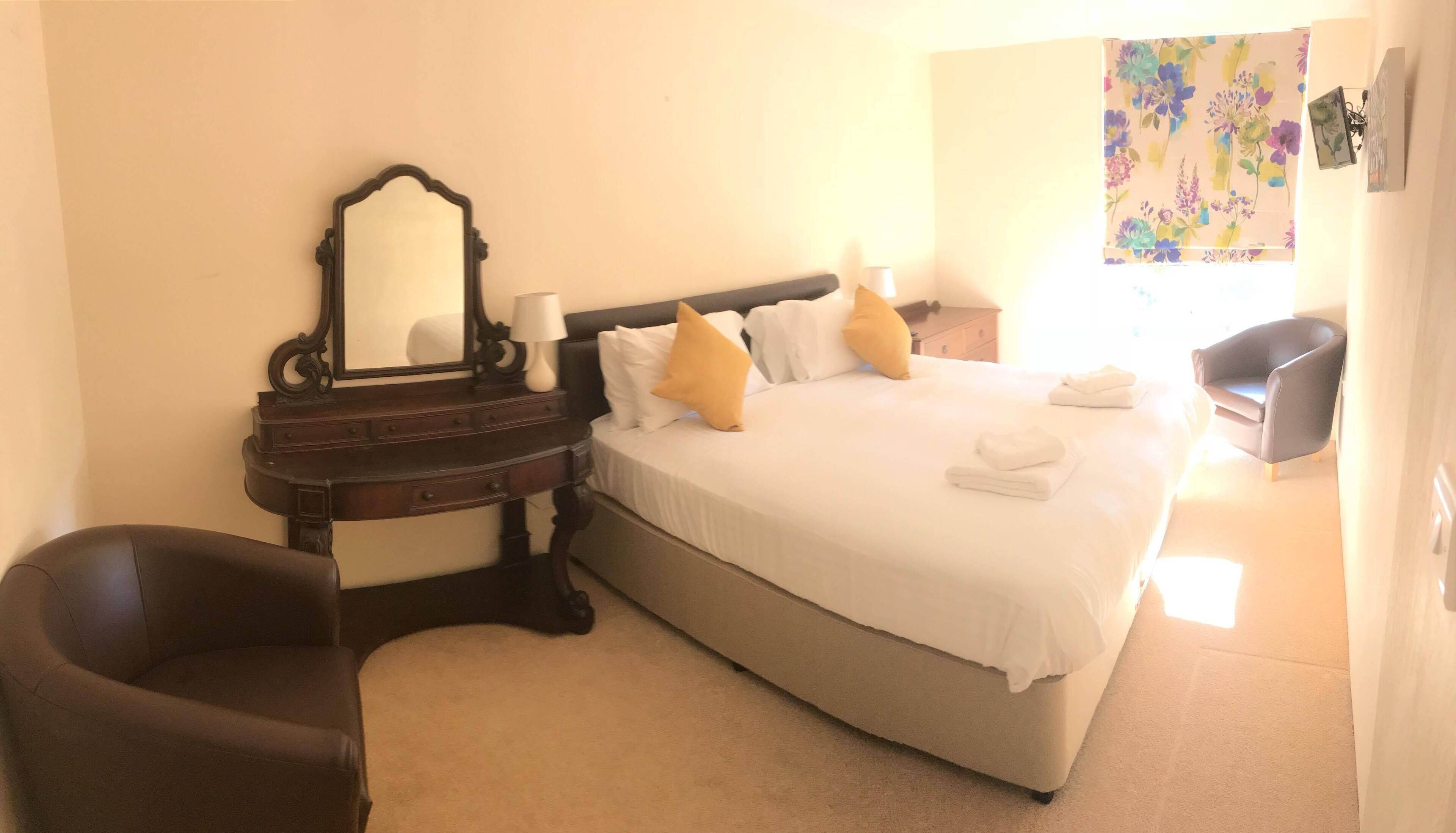 A hotel room with a bed, a nightstand, a dresser, a chair, and a mirror.