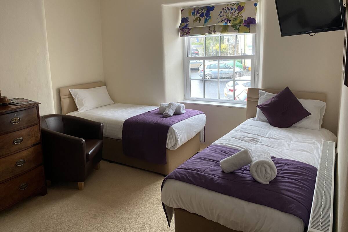 A hotel room with two beds, a desk, a chair, a dresser, and a TV.