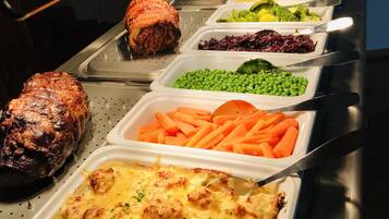Un bufé con diversos platos, incluyendo carne asada, guisantes verdes, zanahorias y un pastel de carne.