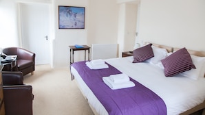 A hotel room with a bed, a desk, a chair, a radiator, and a painting on the wall. - The Poltimore Inn (South Molton)