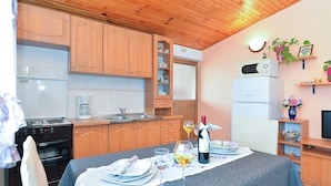 A compact kitchen with wooden cabinets, a built-in oven, and a microwave. There's a dining table set with plates, glasses, and a bottle of wine. - Apartment 2018/28685 (Istria - Pula), 2500m from the beach (Pula)