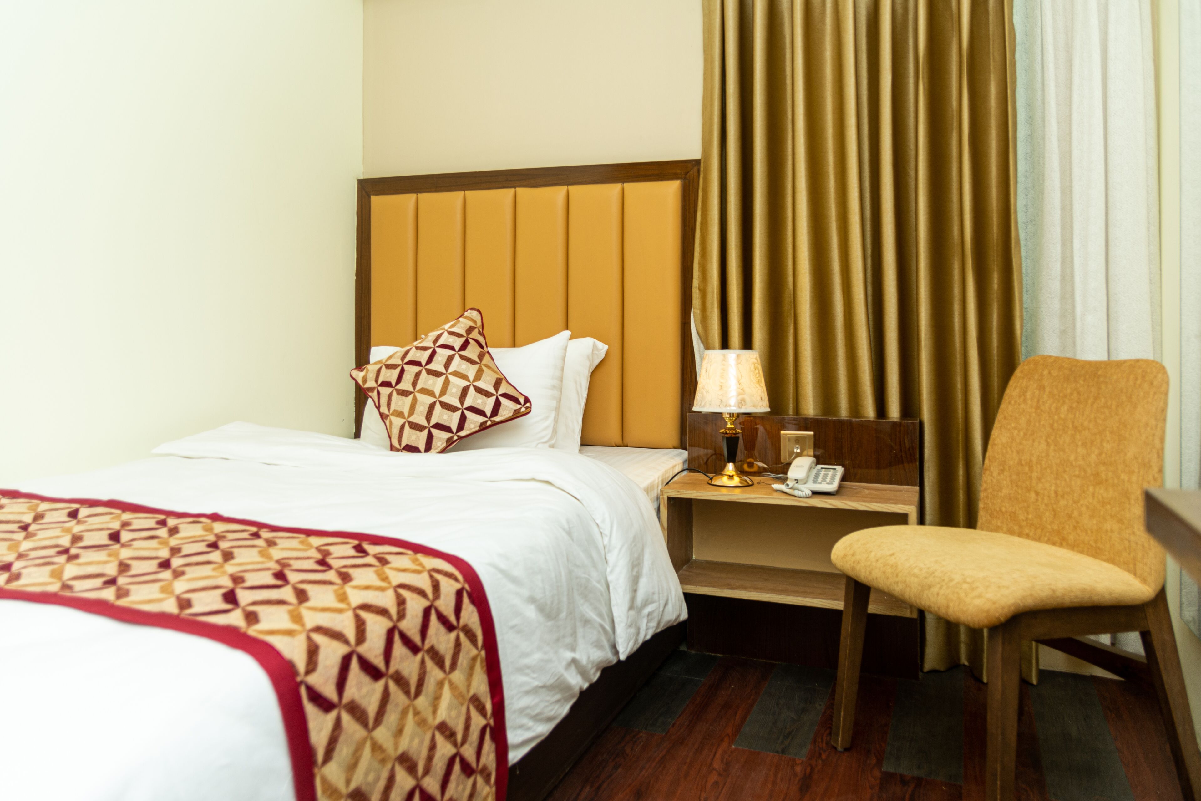 A hotel room with a bed, a chair, a nightstand with a lamp, and curtains.