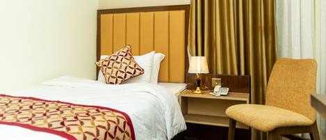 A hotel room with a bed, a chair, a nightstand with a lamp, and curtains.