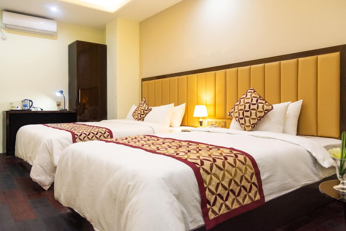 A hotel room with two beds, a nightstand, a lamp, and a vase with flowers.