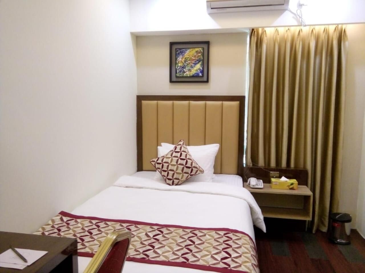 Une chambre d’hôtel comprenant un lit, une table de chevet avec un téléphone et une boîte de mouchoirs, un bureau avec une chaise et une fenêtre avec des rideaux.