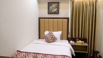Une chambre d’hôtel comprenant un lit, une table de chevet avec un téléphone et une boîte de mouchoirs, un bureau avec une chaise et une fenêtre avec des rideaux.