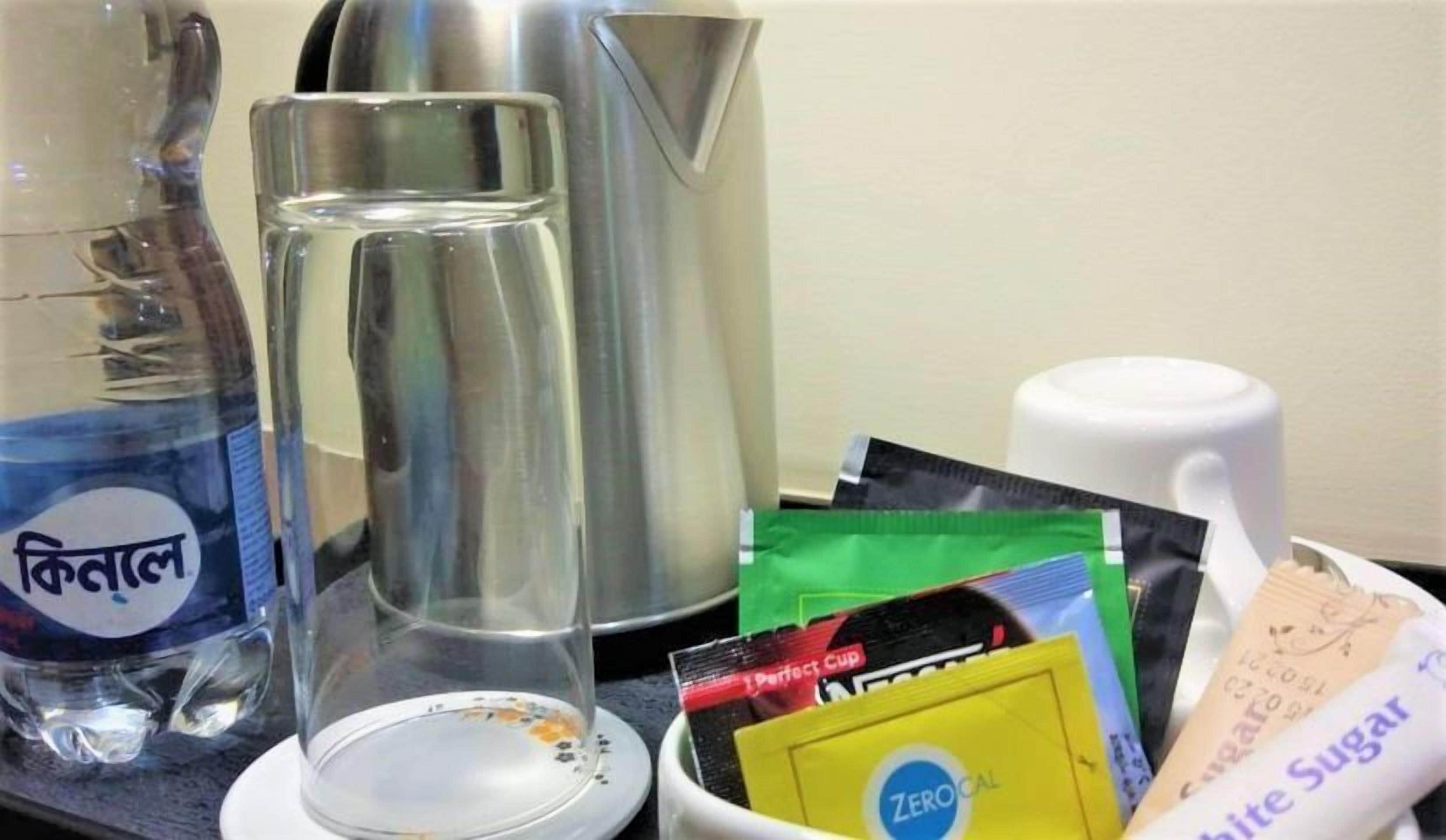 A kitchen counter with a kettle, a glass, and packets of sugar and tea.