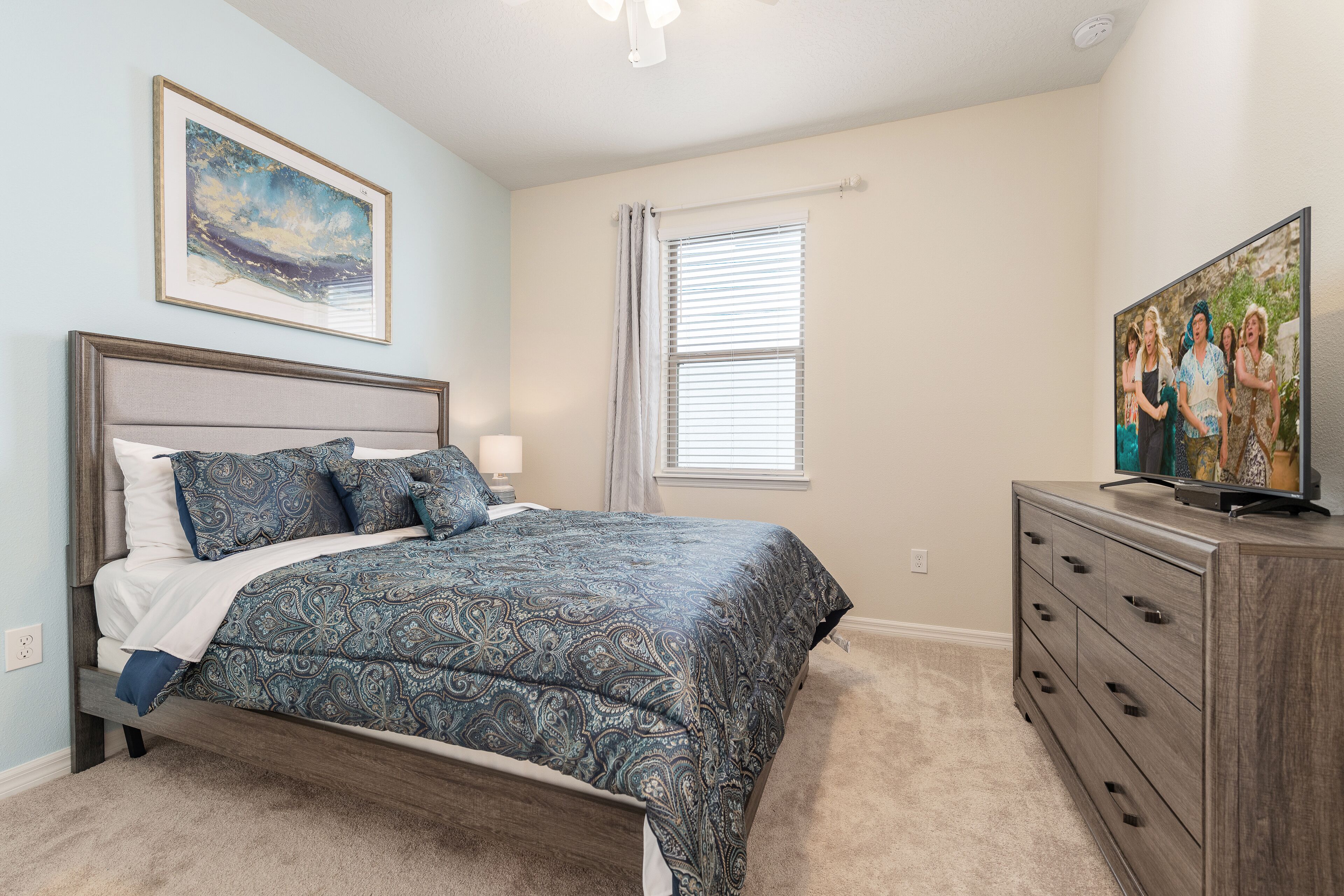 A bedroom with a bed, a dresser, a painting, and a window with blinds.