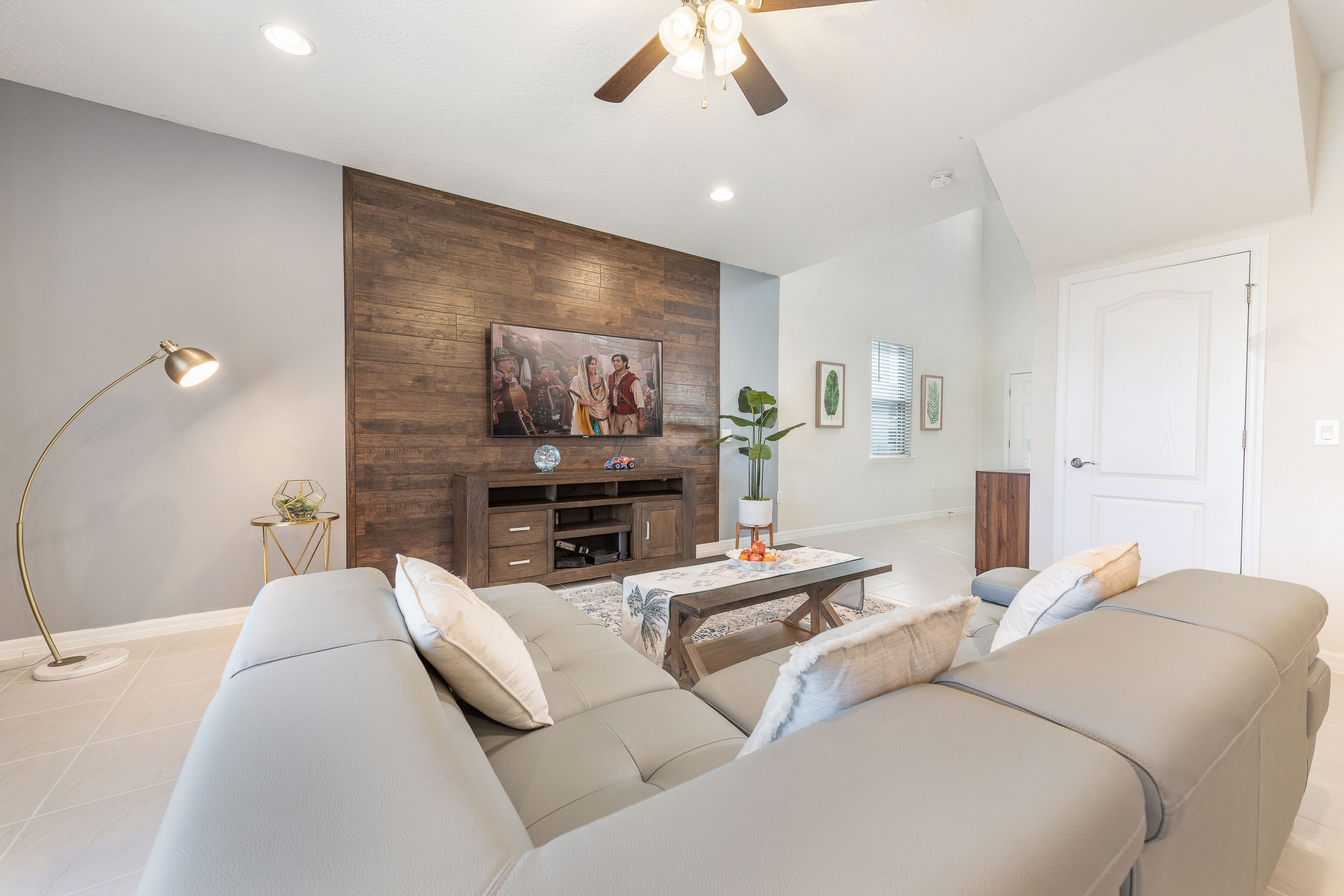 Ein modernes Wohnzimmer mit einer Eckcouch, einer Holz-Unterhaltungseinheit und einem Deckenventilator.