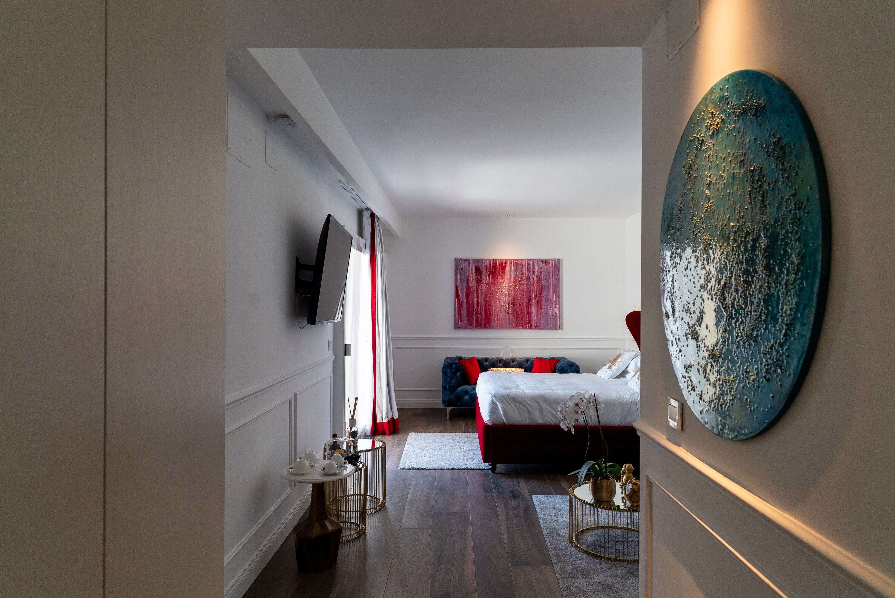 A modern bedroom with a large bed, a TV, and a red abstract painting.