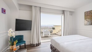 A hotel room with a large bed, a TV, a desk with a chair, a view of the city, and a balcony with outdoor seating. - Monastero dei Santi (Rome)