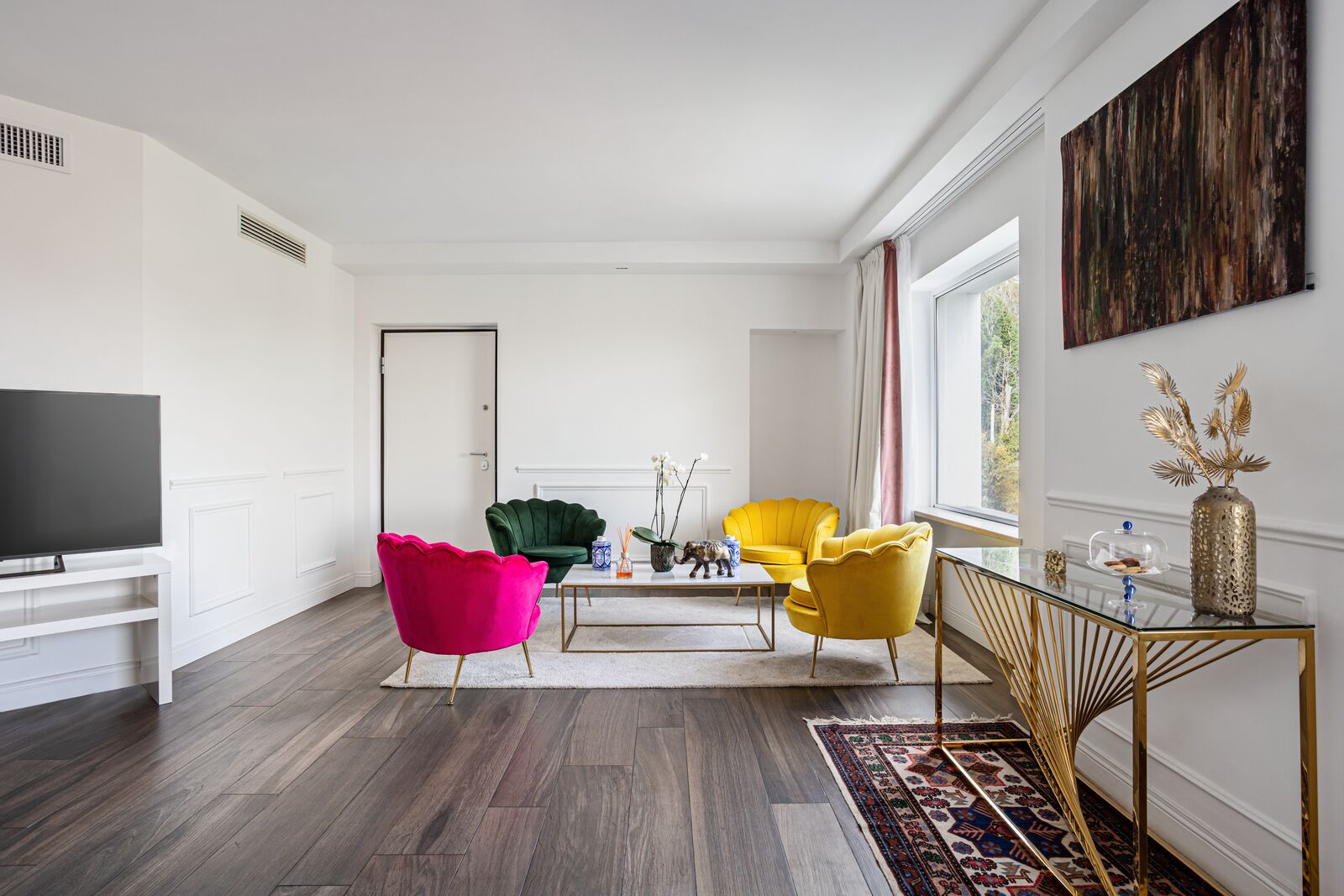 Una sala de estar moderna con un televisor de pantalla plana, un sillón verde, un sillón amarillo y una silla rosa llamativa.