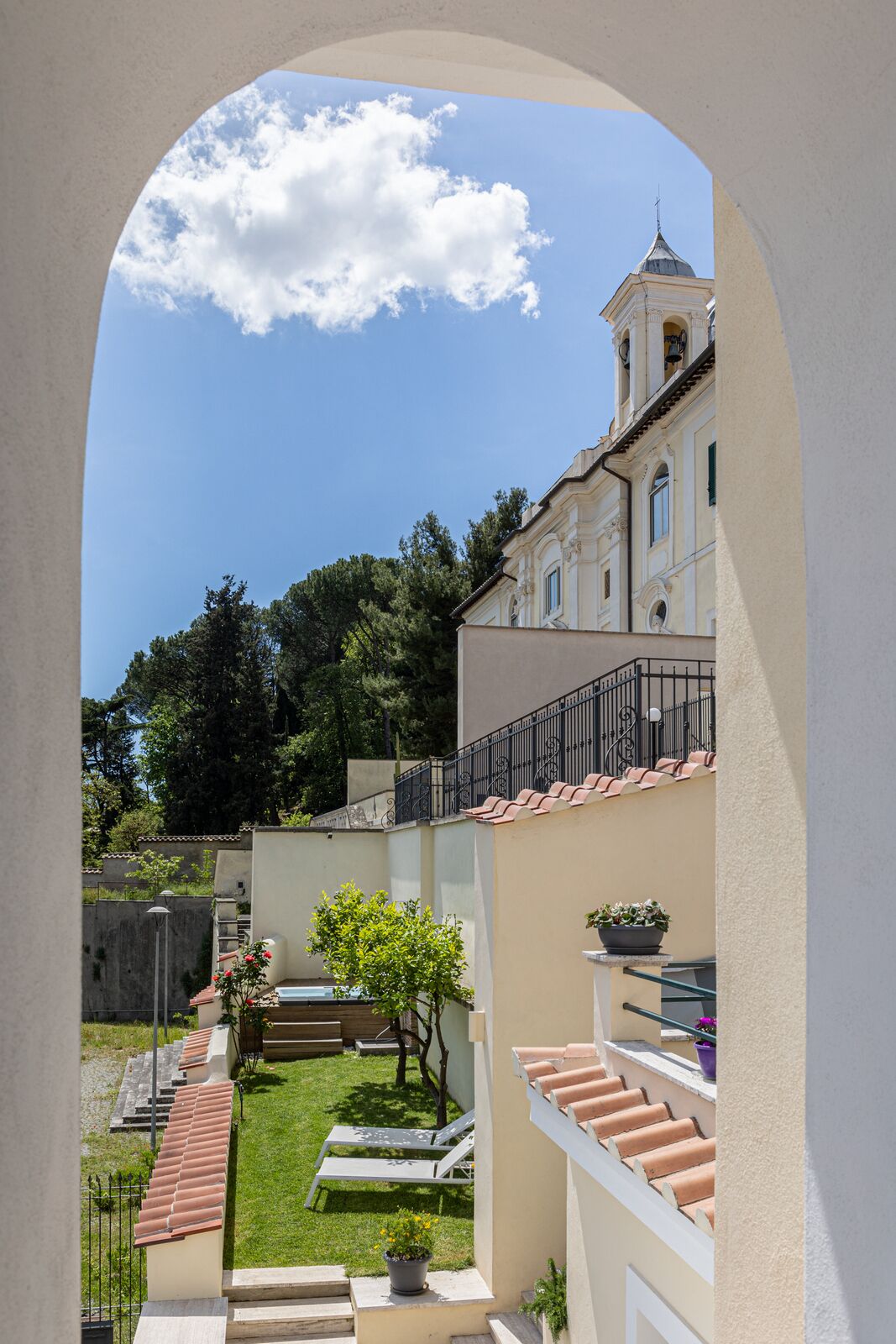 Une cour offrant une vue sur un bâtiment doté d’un clocher, entouré de verdure et surplombant un ciel dégagé.