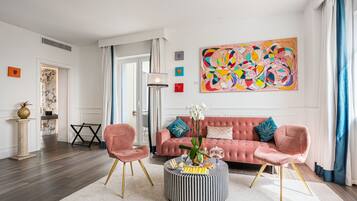 A modern living room with a pink sofa, two pink chairs, a striped ottoman, and a colorful abstract painting.