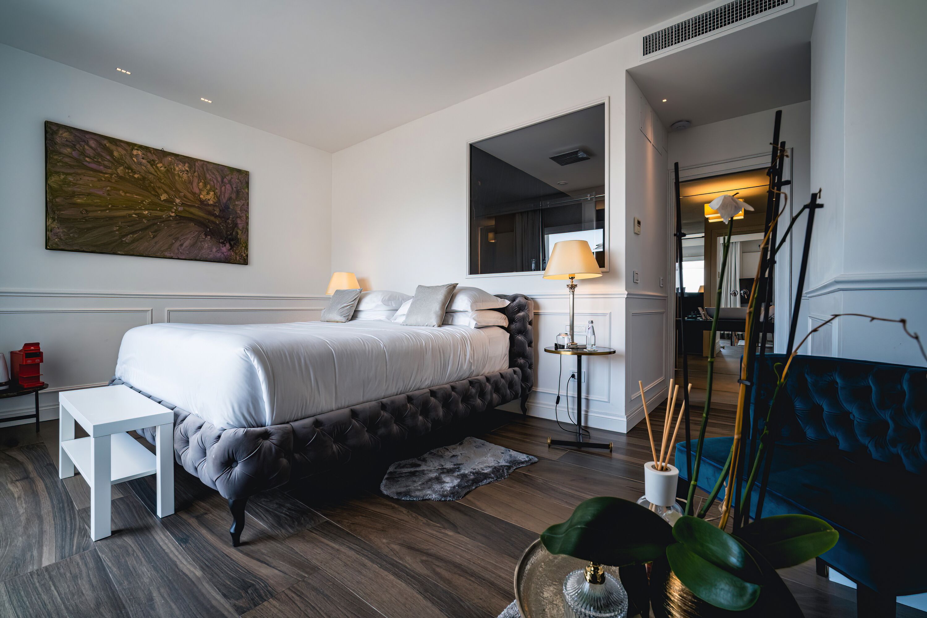 Un dormitorio moderno con una cama grande, mesitas de noche, un banco, una lámpara de pie y un espejo.