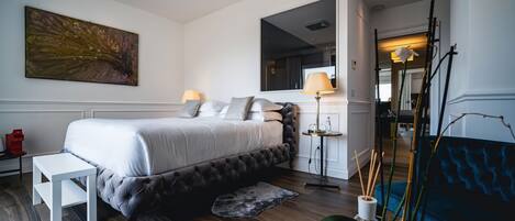 Un dormitorio moderno con una cama grande, mesitas de noche, un banco, una lámpara de pie y un espejo.