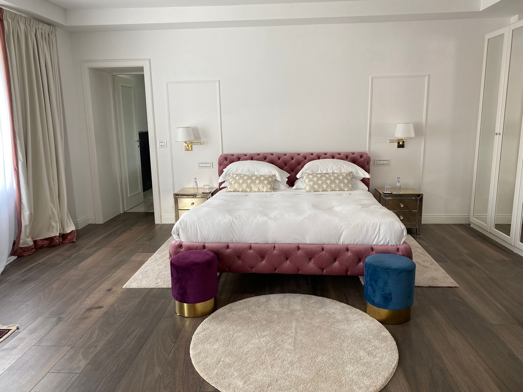 Un dormitorio con una cama grande, dos mesitas de noche, un tapete redondo y un armario.