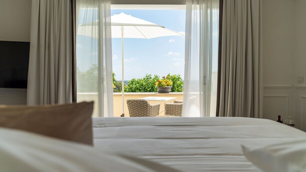 A hotel room with a bed, a TV, a balcony with a table and chairs, and a potted plant. - Monastero dei Santi (Rome)