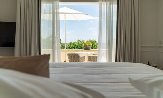 A hotel room with a bed, a TV, a balcony with a table and chairs, and a potted plant.
