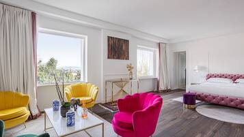 A hotel room with a bed, two yellow armchairs, a pink armchair, a white coffee table, and a view of the outdoors.