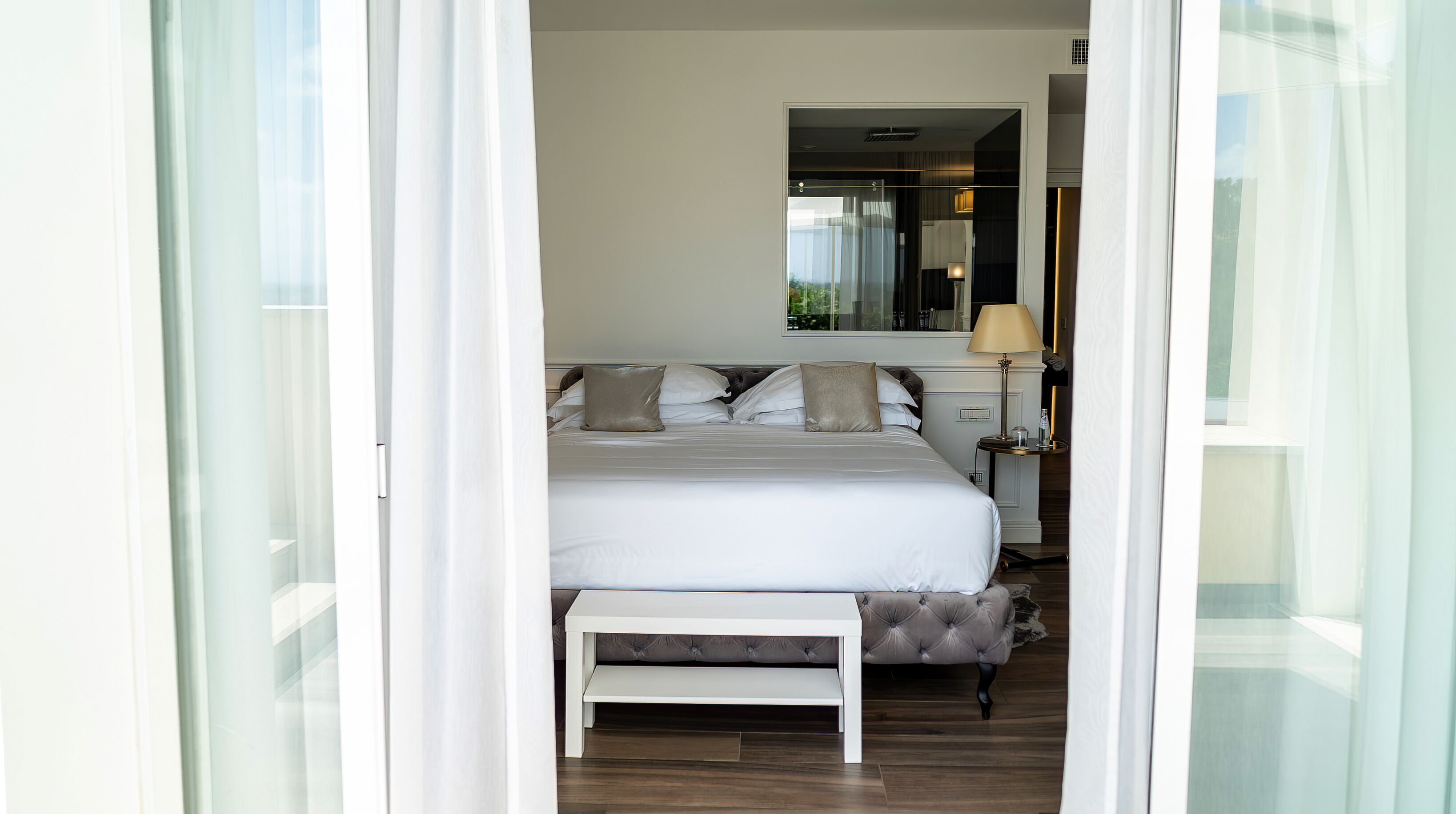 A bedroom with a bed, bedside table, lamp, and a mirror.