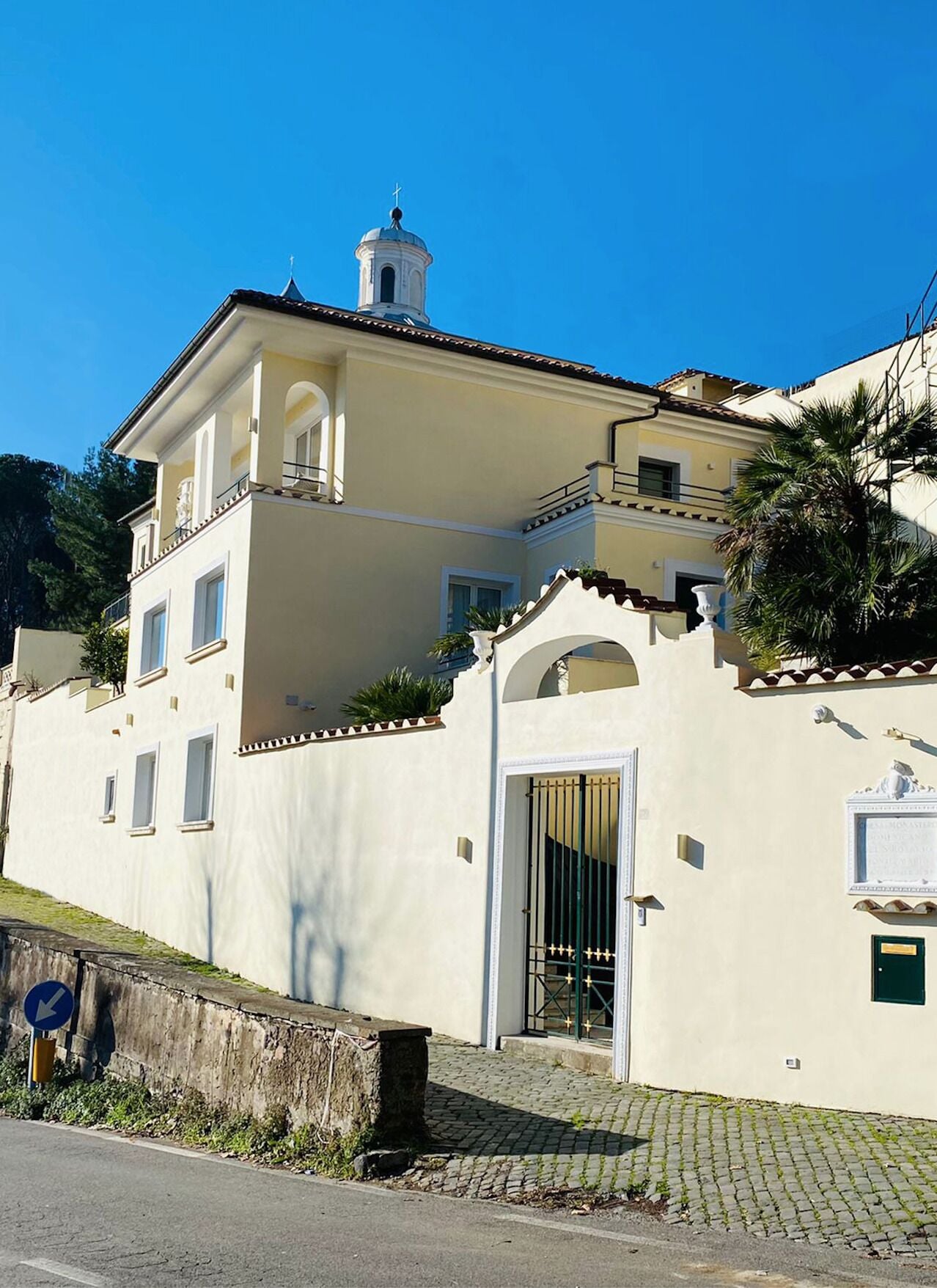 Un edificio de dos pisos con fachada blanca, un balcón y una pequeña torre con una cruz en la parte superior.