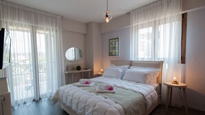 Ein Schlafzimmer mit einem großen Bett, einem Nachttisch, einem Spiegel und einem Fenster mit transparenten Vorhängen.