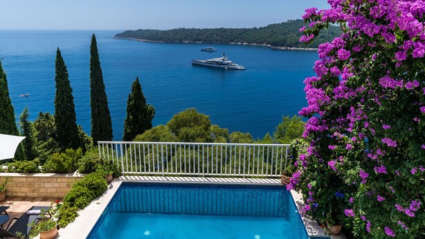 A pool with a view of the sea and boats, surrounded by greenery and cypress trees. - Villa Adrian (Dubrovnik)