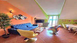 A living room with a blue sofa, yellow chairs, a dining table, and a TV. - Villa Adrian (Dubrovnik)
