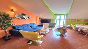 A living room with a blue sofa, yellow chairs, a dining table, and a TV.