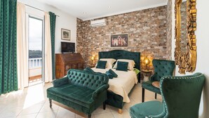 A bedroom with a stone wall, a bed with green bedding, a green sofa, a chair, and a wooden dresser. - Villa Adrian (Dubrovnik)