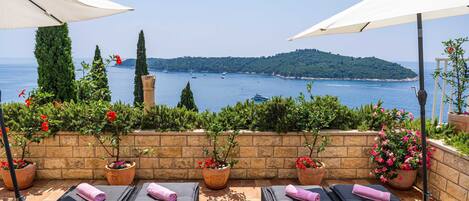 A terrace with lounge chairs, potted plants, and umbrellas overlooking a body of water.