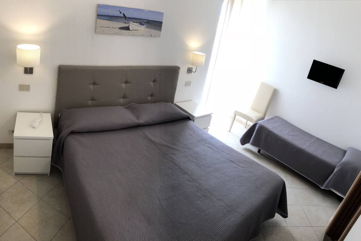 Een slaapkamer met een bed, nachtkastjes, een stoel en een schilderij aan de muur.