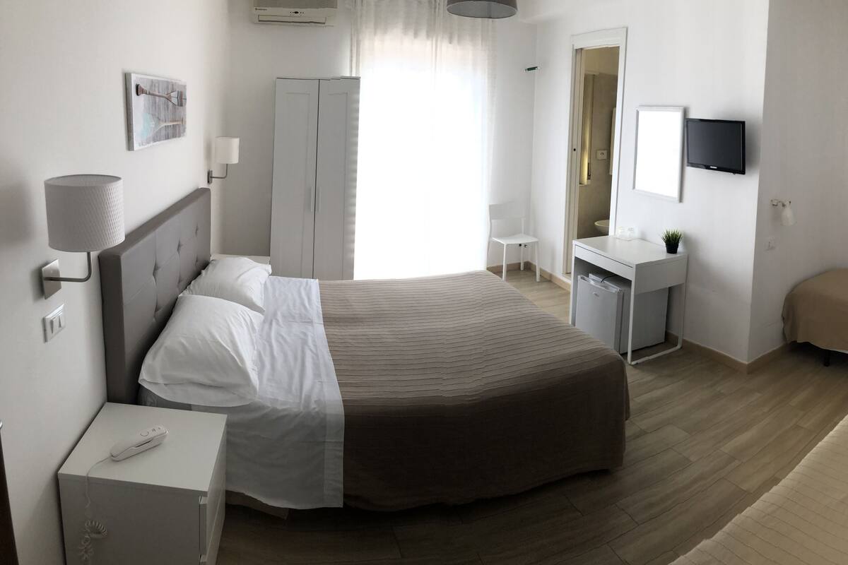 Een moderne hotelkamer met een groot bed, nachtkastje, bureau, stoel en een aan de muur bevestigde televisie.