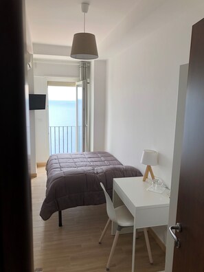A bedroom with a bed, a desk with a chair, a lamp, and a TV on the wall.