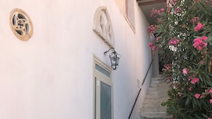 A staircase with a handrail, a door with a glass panel, and decorative wall elements including a circular window and a wall-mounted light fixture. - Villa Jole Taormina (Taormina)