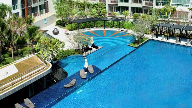 A large outdoor swimming pool with lounge chairs and umbrellas, surrounded by greenery and modern buildings. - SEACRAZE D702 - 1 Bedroom - Near Beach (Hua Hin)