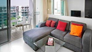 A modern living room with a grey sofa, red and orange cushions, a glass coffee table, and a balcony with a view of other buildings. - SEACRAZE D702 - 1 Bedroom - Near Beach (Hua Hin)